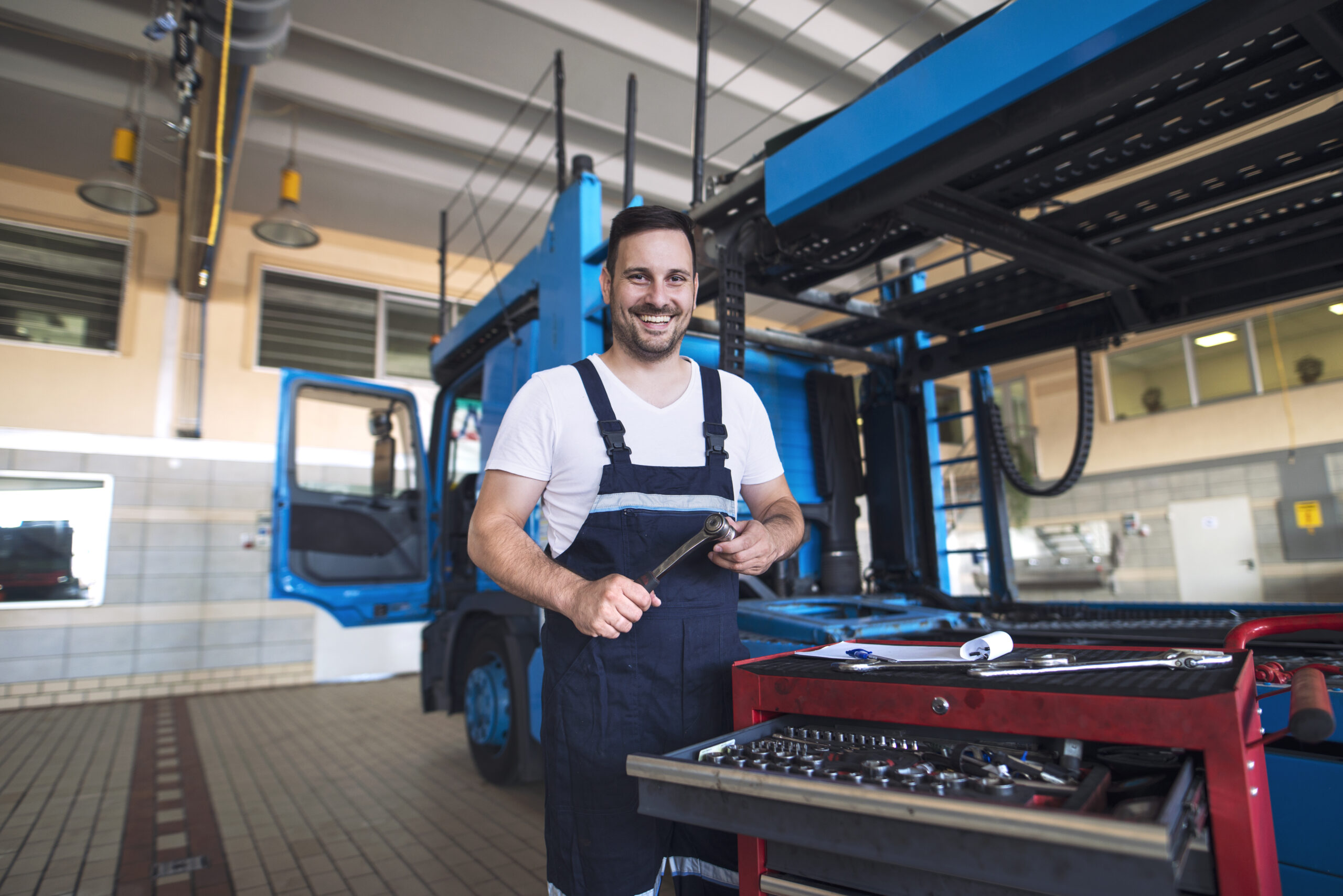 portrait of positive smiling truck serviceman with tools standing by truck vehicle in workshop.