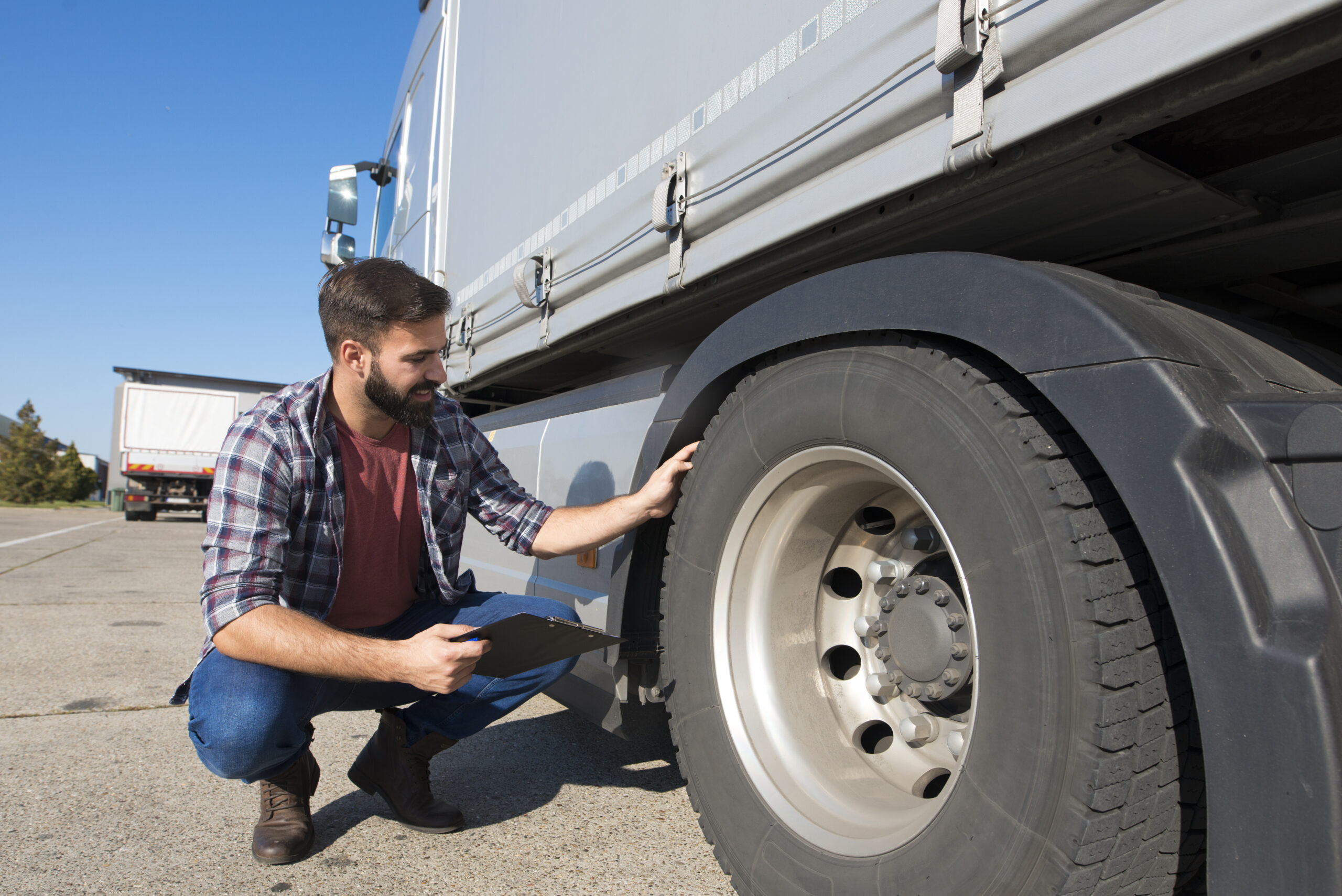 truck driver inspecting tires and checking depth of tire tread for safe ride.